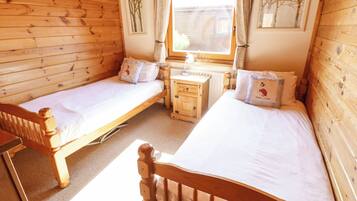 A wooden cabin room with two single beds, a wooden nightstand, and a window with curtains.