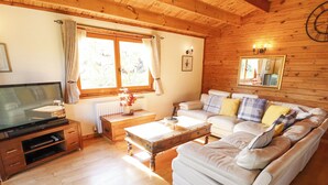 Un salon chaleureux avec un plafond en bois, un ensemble de canapés, une table basse, un téléviseur et une fenêtre avec des rideaux.