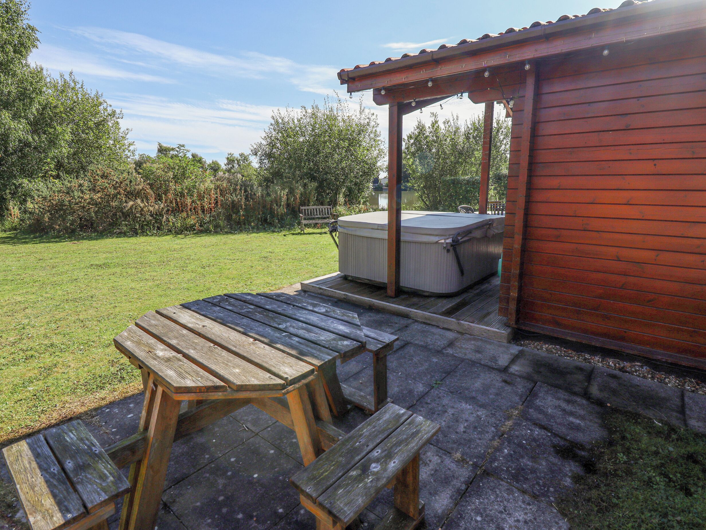 A wooden deck with picnic tables and a hot tub under a wooden pergola.