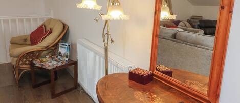 A room with a wooden curved table, a chair, a floor lamp, a mirror, and a radiator.