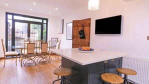 Una cocina moderna con una isla grande, taburetes de bar, un área de comedor con sillas y un televisor montado en la pared.