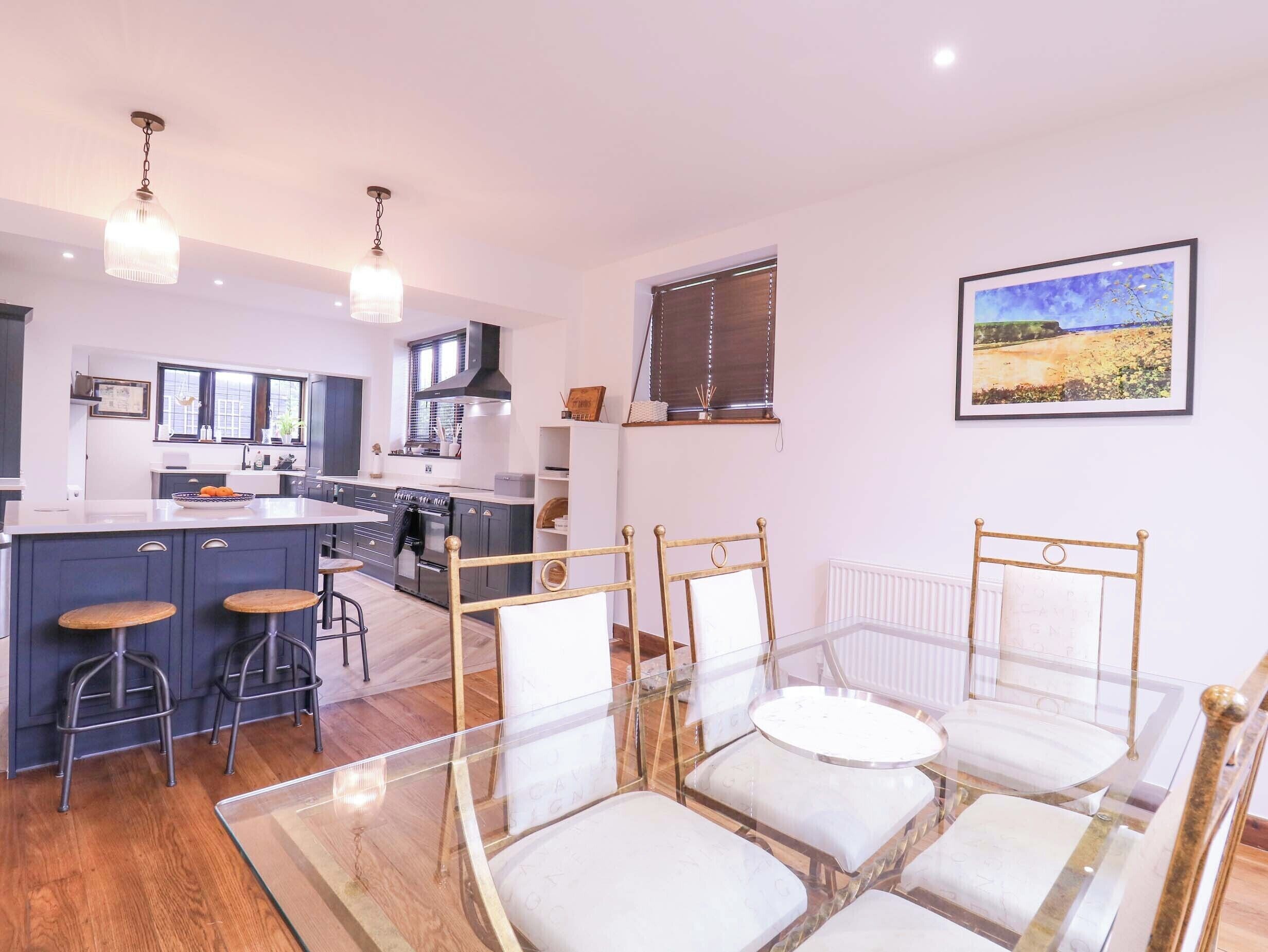 A modern kitchen with a central island, bar stools, and a glass dining table with chairs.