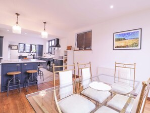 Et moderne køkken med en central ø, barstole og et glasbord med stole.