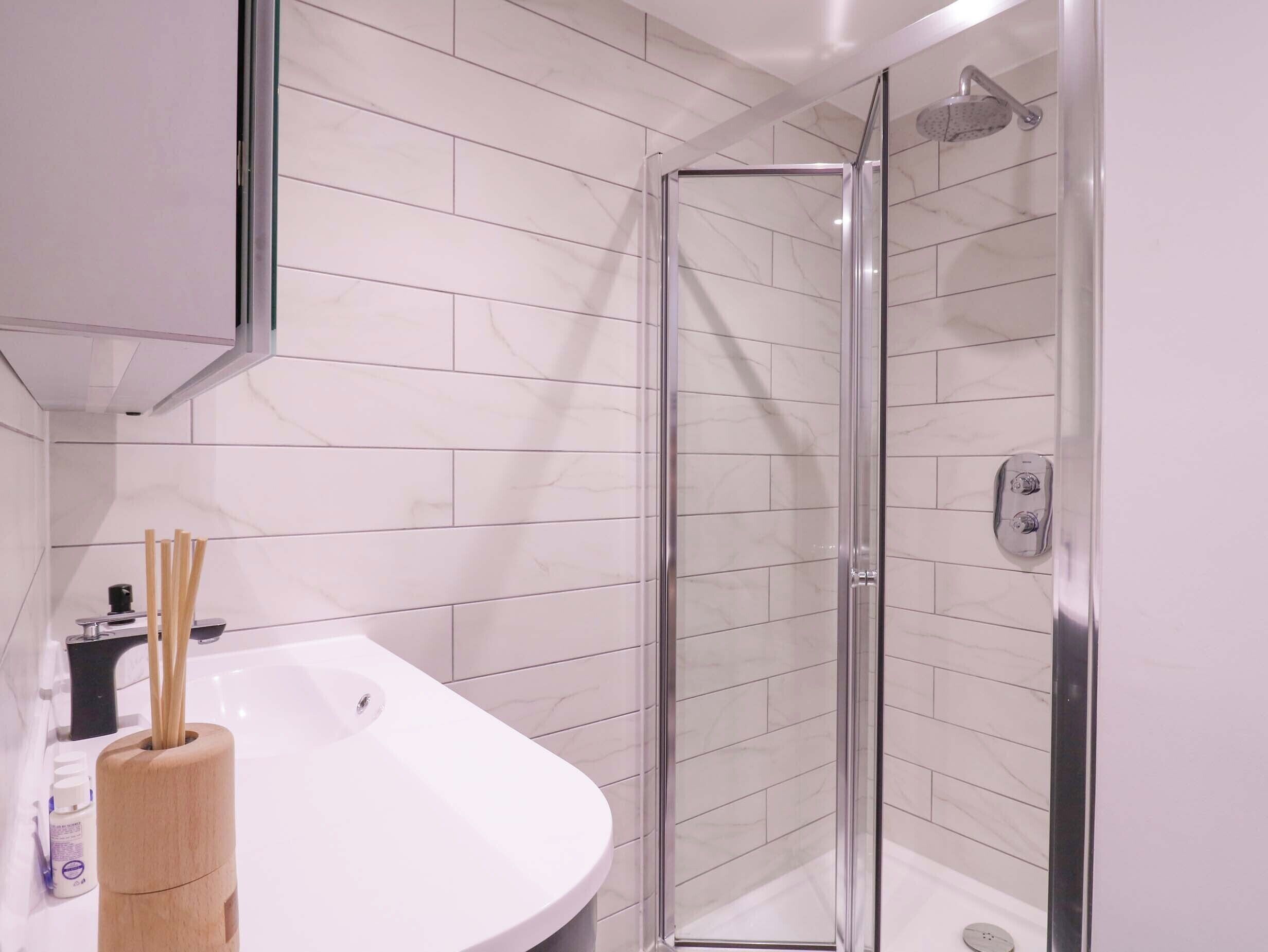 Un baño moderno con ducha envuelta en vidrio, un lavabo blanco y un soporte de madera para cepillos.