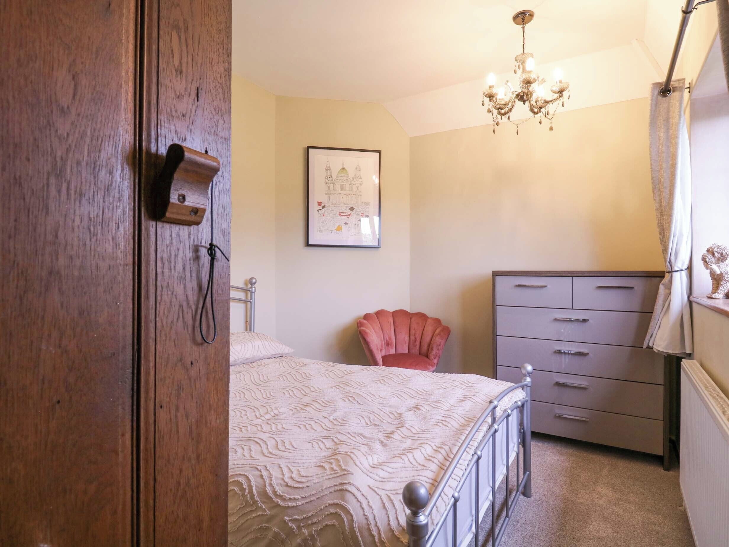 Une chambre à coucher comprenant un lit, une commode, une chaise, un lustre et une carte encadrée accrochée au mur.