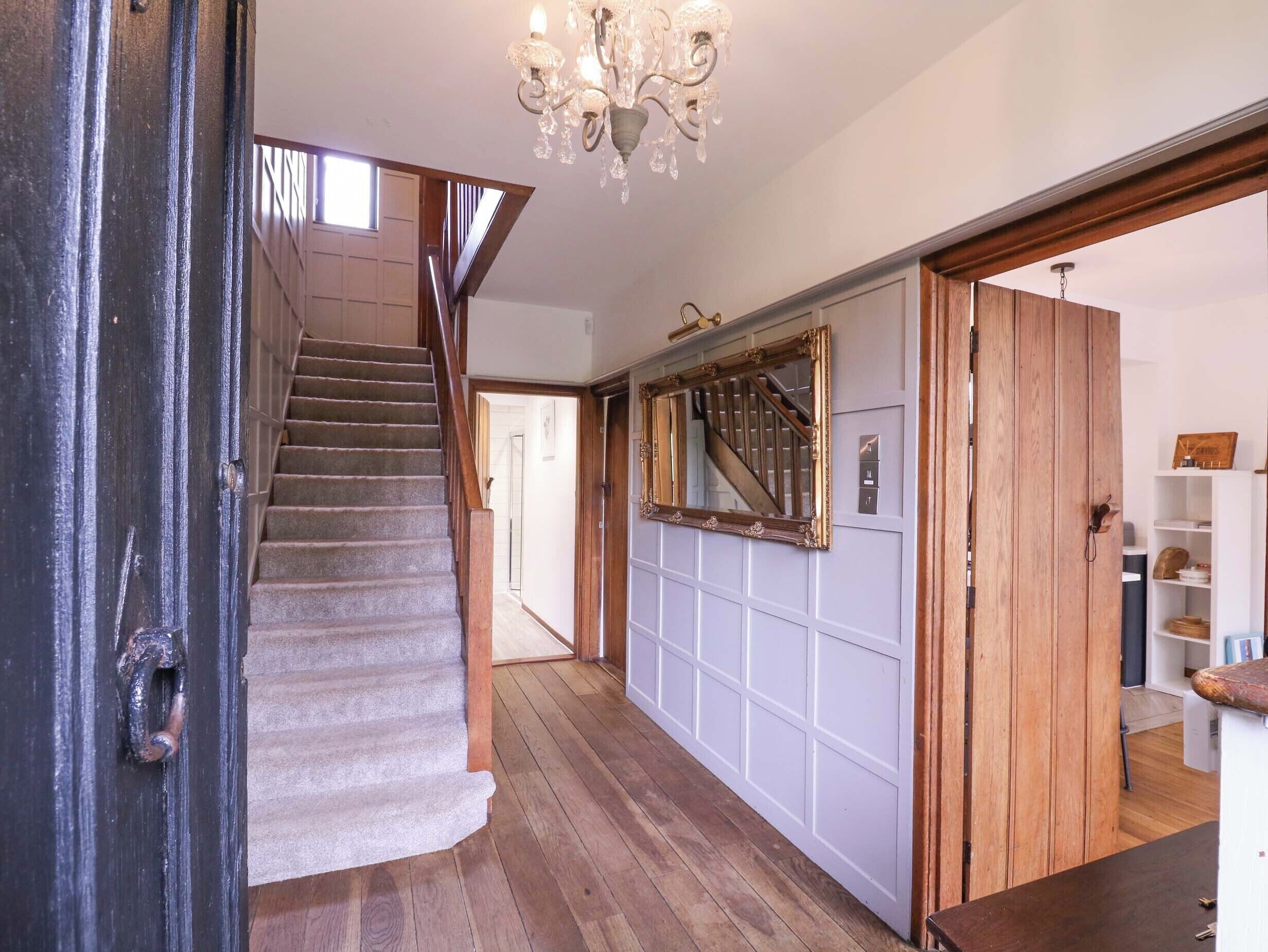 A staircase with wooden steps and a handrail, leading to a landing with a white paneled wall and a large mirror.