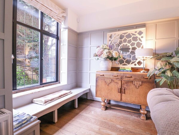 A room with a wooden bench, a cabinet with decorative items, and a window with a view of greenery. - Home by the Sea (Clacton-on-Sea)
