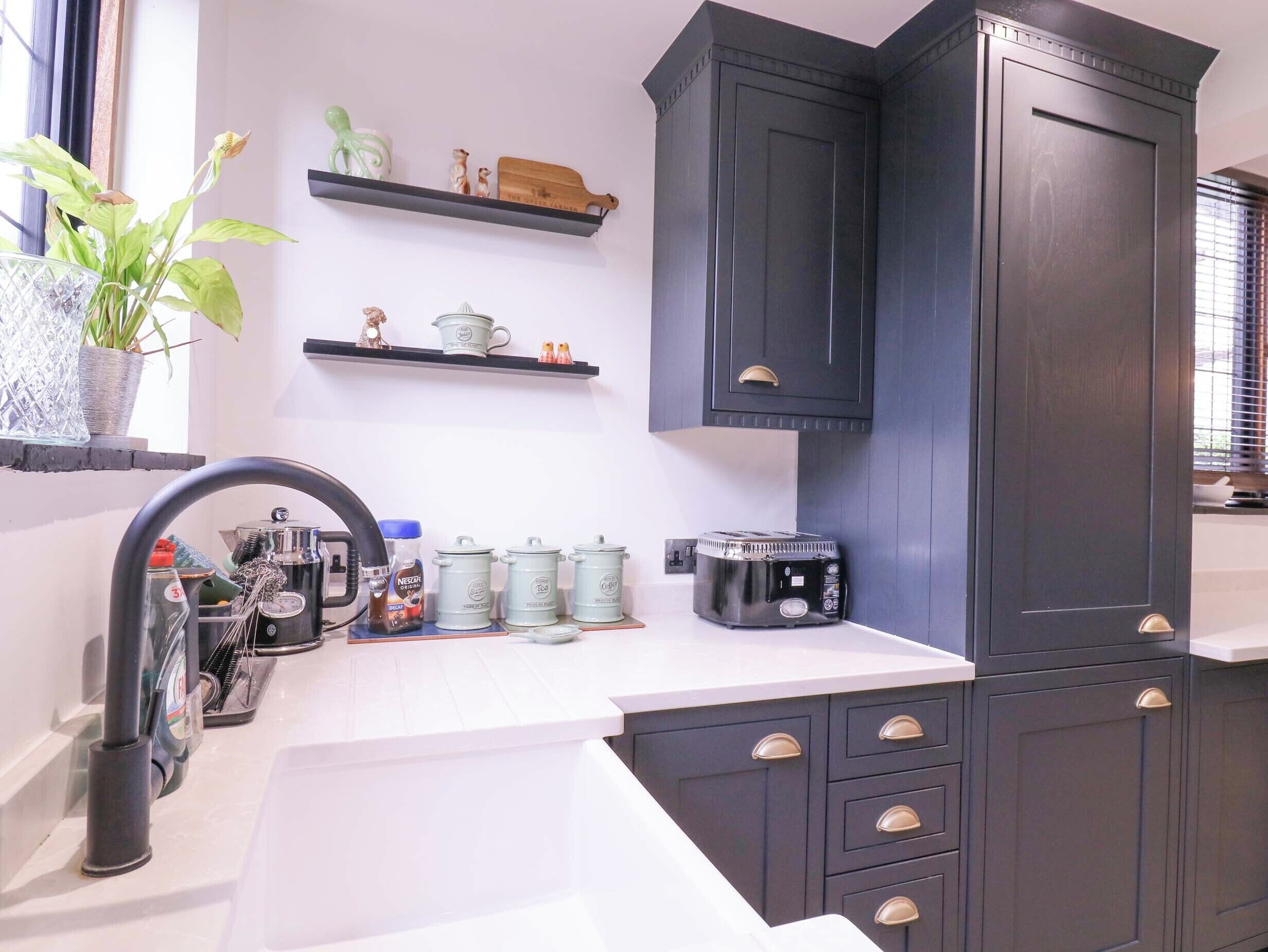 A kitchen with dark cabinets, a white countertop, and a window with a plant.