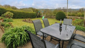 Een terras met een tafel en stoelen, omgeven door een tuin met verschillende planten en een schommel.