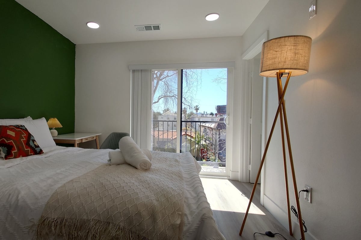 Une chambre à coucher avec un lit, une table de chevet, une lampe et une vue sur l’extérieur.