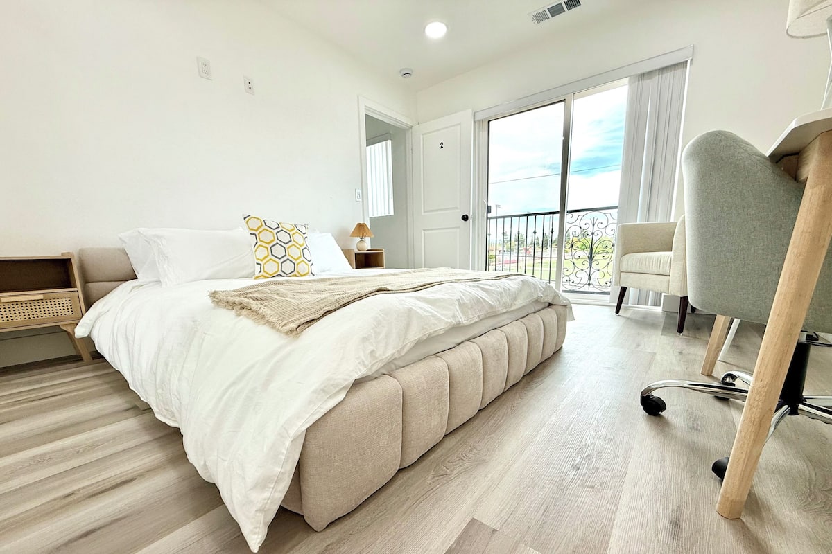 Une chambre avec un grand lit, une chaise, une petite table et un balcon avec vue.