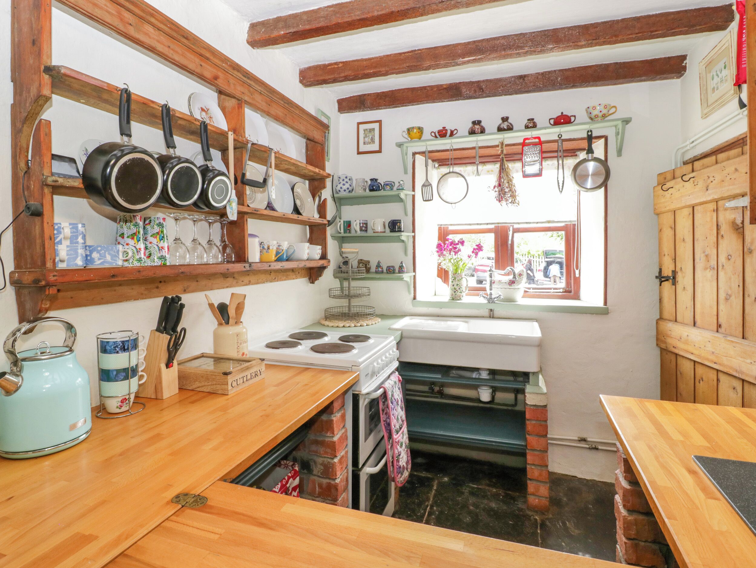 A kitchen with wooden beams, a stove, a sink, and various kitchen utensils.