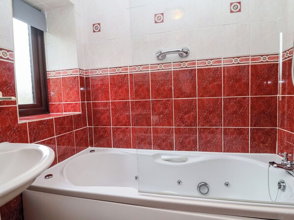 A bathroom with a bathtub, a sink, and red marble tiles. - The Hayloft Cottage Apartment (Lyme Regis)