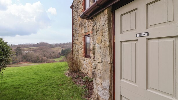 A stone building with a laundry sign, a green field, and a distant view of hills. - The Hayloft Cottage Apartment (Lyme Regis)
