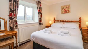 A neatly arranged bedroom with a bed, bedside tables, a mirror, and a window with curtains. - The Hayloft Cottage Apartment (Lyme Regis)