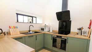 Een moderne keuken met groene kastjes, een zwarte kookplaat, een magnetron en een spoelbak.