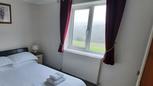 A hotel room with a bed, a nightstand, a window with curtains, and a view of the outdoors. - The Goathouse Cottage (Lyme Regis)
