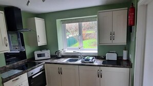 A kitchen with white cabinets, a microwave, a kettle, and a window with a view of the outside. - The Goathouse Cottage (Lyme Regis)