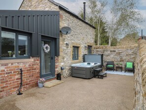 A stone house with a modern design, featuring a hot tub, outdoor seating, and a brick wall. - The Bottling Shed (Matlock)
