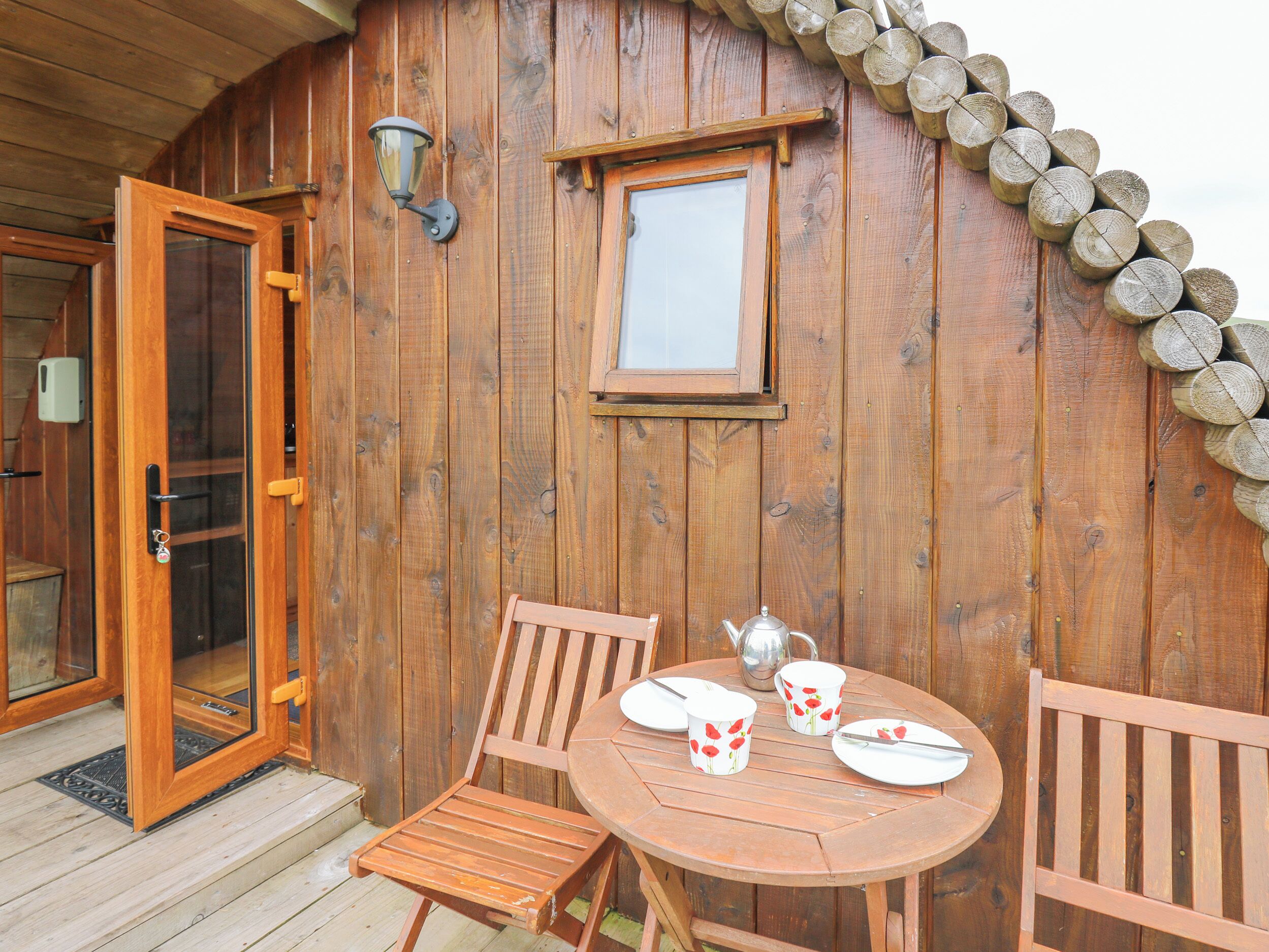 A wooden cabin with a glass door, a small table with a teapot and cups, and a window with a wooden frame.