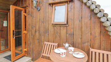 A wooden cabin with a glass door, a small table with a teapot and cups, and a window with a wooden frame.