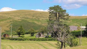 A rural landscape with rolling hills, a large tree, and a small house with a sloped roof. - Oak View (Llangadog)