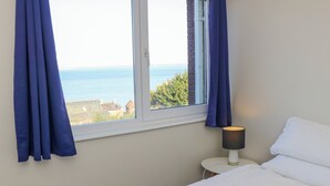 Ein Schlafzimmer mit Bett, Nachttischlampe, einem Fenster mit Vorhängen und Meerblick.