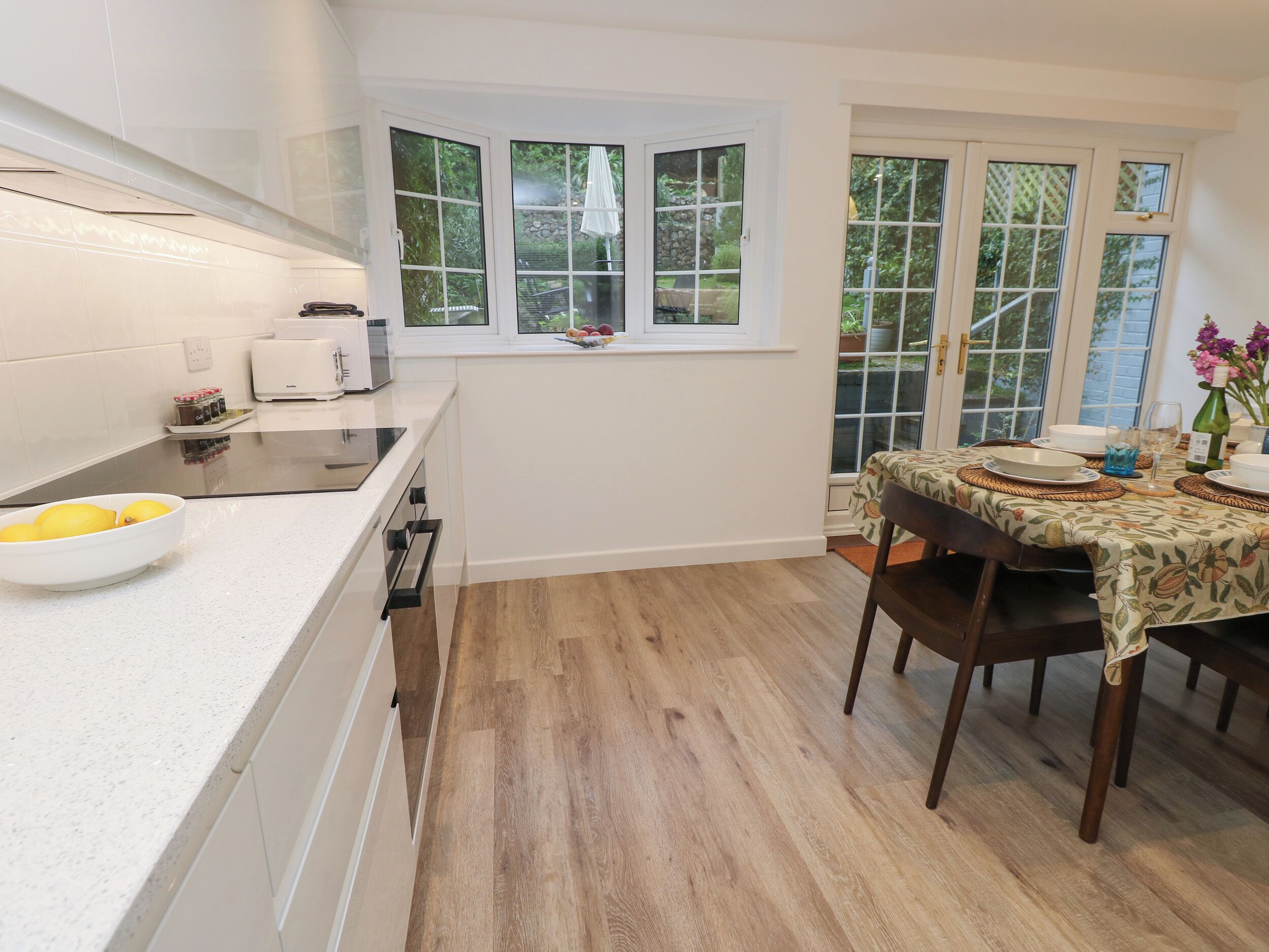 Une cuisine moderne avec des meubles blancs, un plan de travail et un coin repas avec une table mise pour deux personnes.