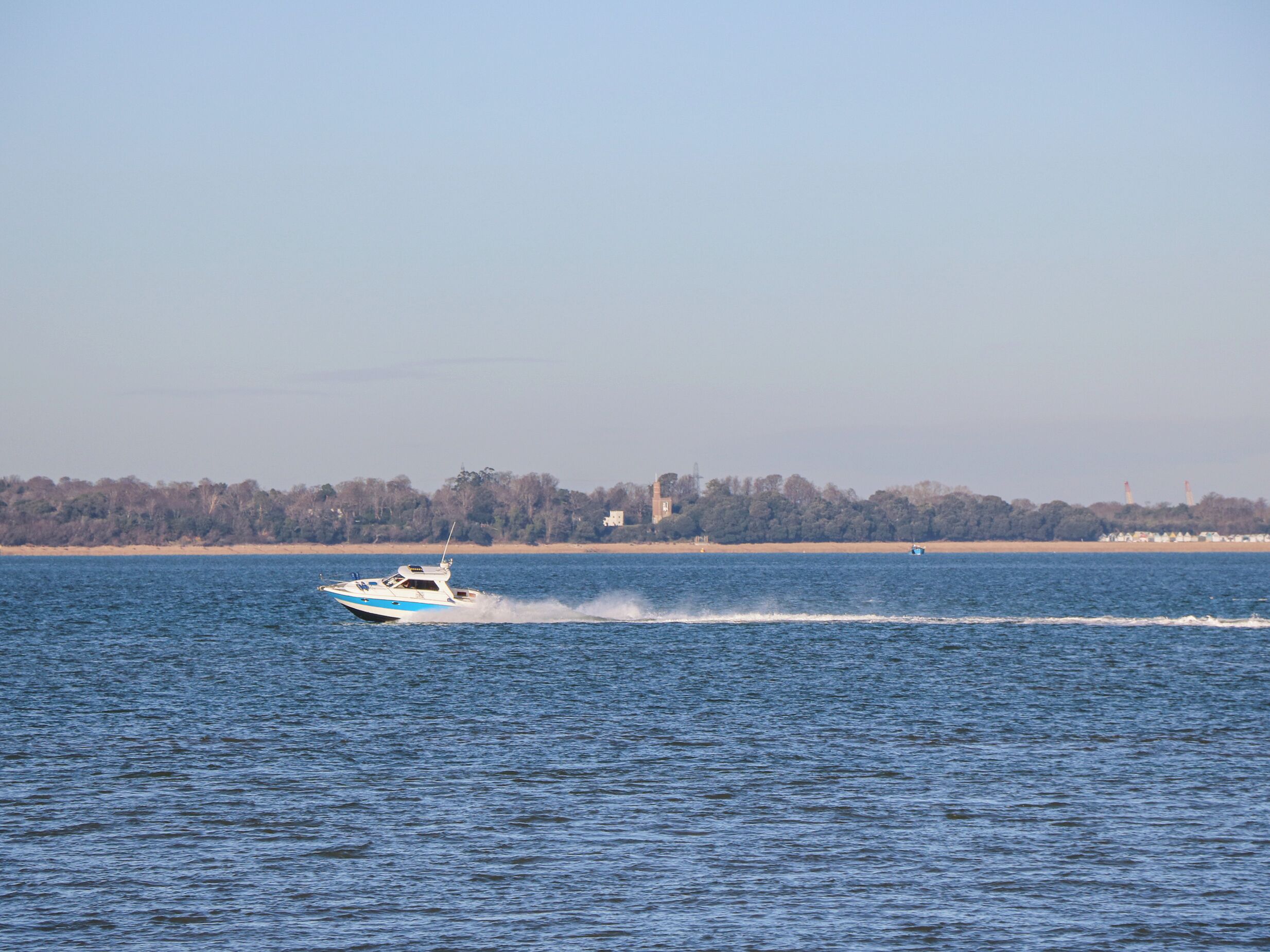 Een boot vaart over een rustig wateroppervlak, met een verre kustlijn op de achtergrond.