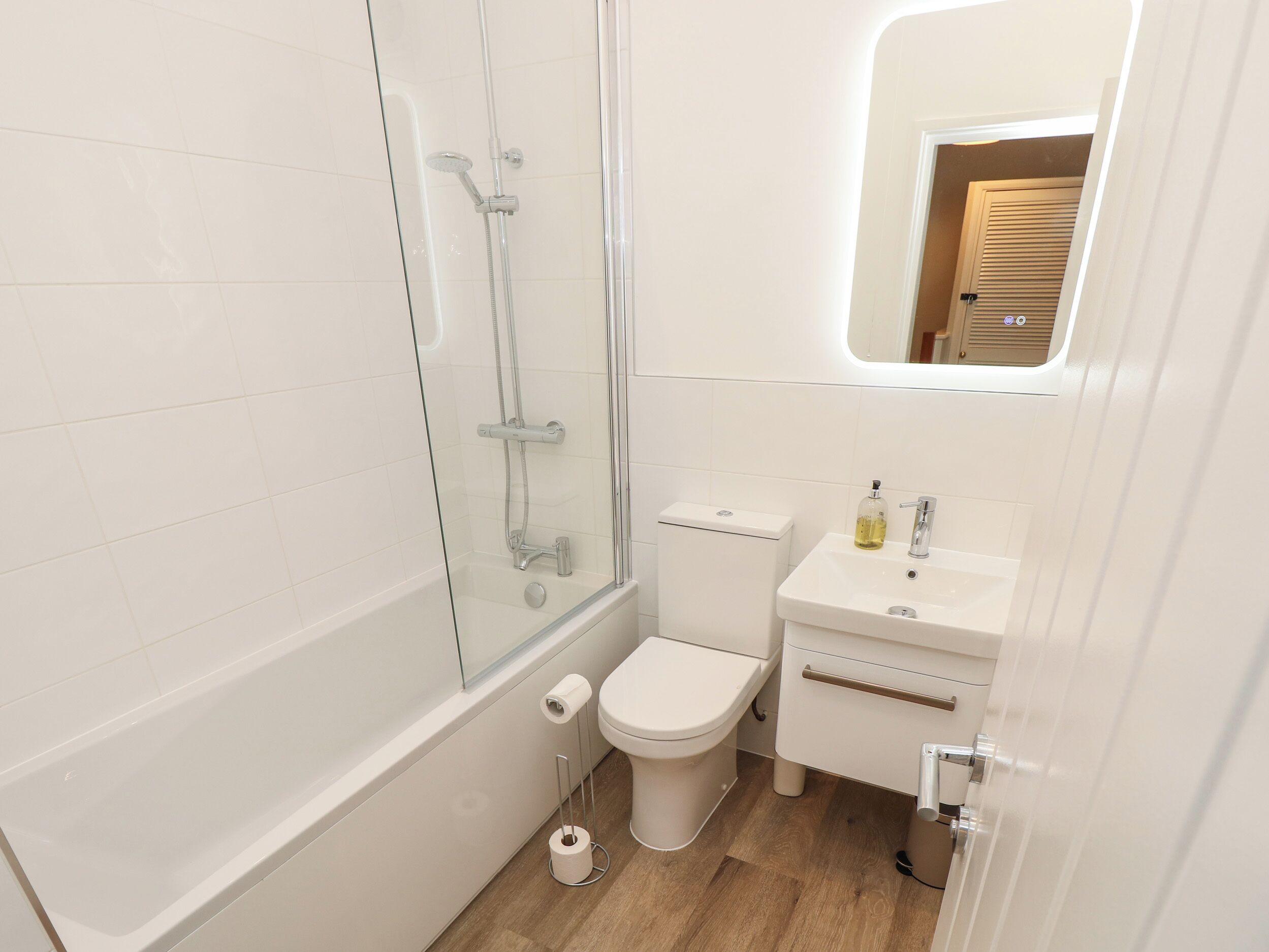 A small, modern bathroom with a glass shower enclosure, a toilet, and a sink with a mirror above it.