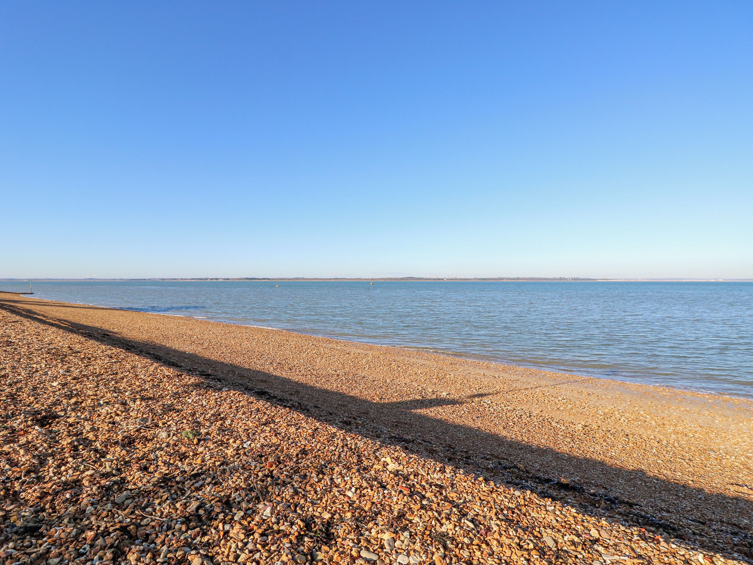 A pebbled beach with calm water and a clear sky.