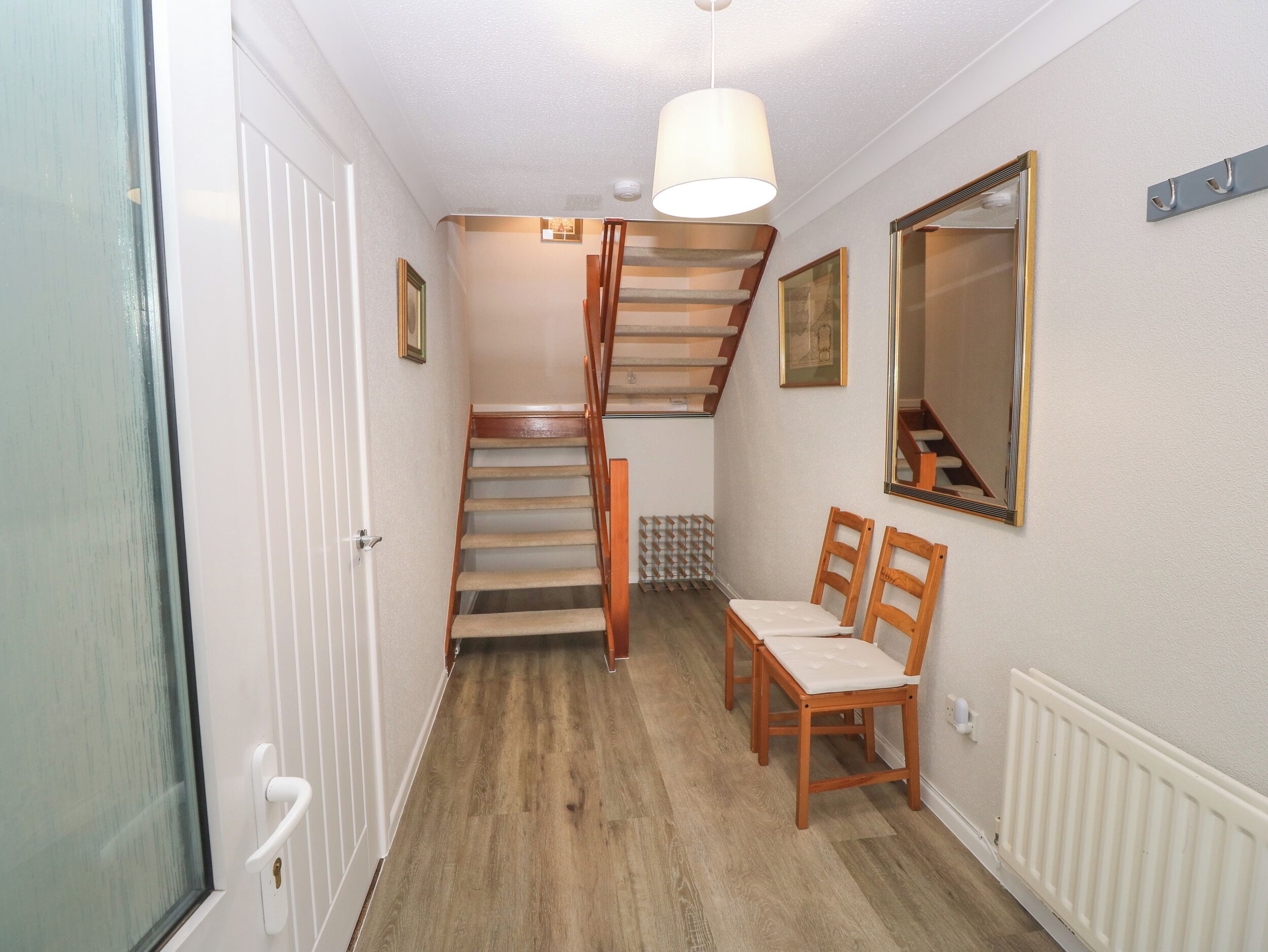 Un couloir avec un escalier en bois, un radiateur blanc et un miroir accroché au mur.