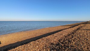 Ein Kiesstrand mit blauem Himmel und ruhiger See.
