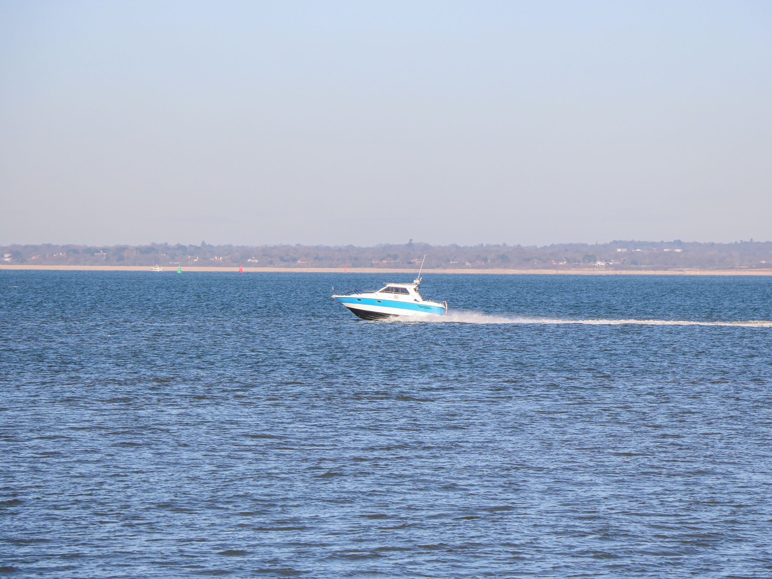 Um barco navegando em uma grande extensão de água, com a costa ao fundo.