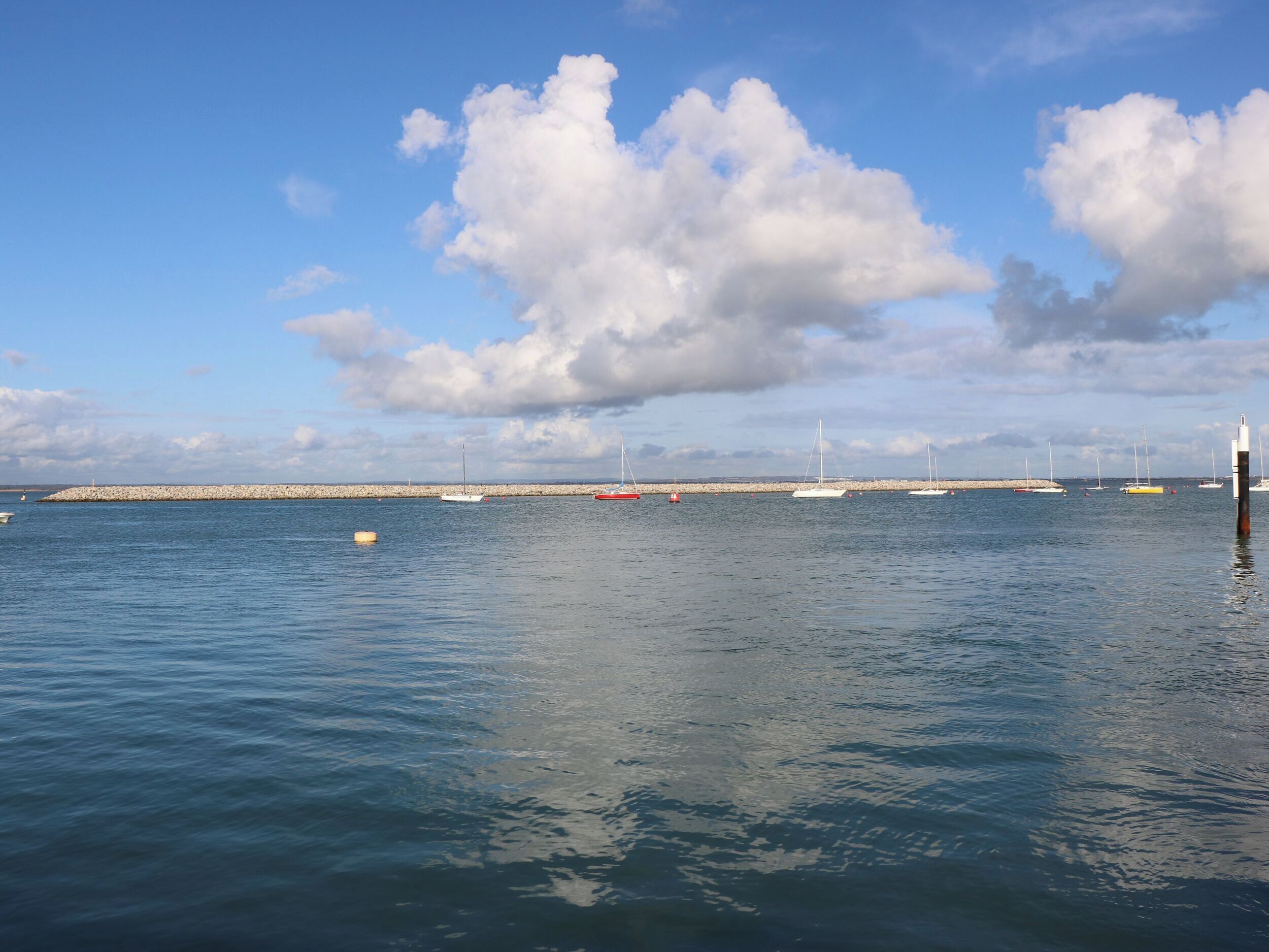 Un puerto tranquilo con barcos, un rompeolas y un cielo despejado.