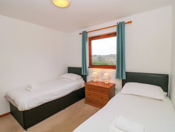 A bedroom with two beds, a wooden dresser, and a window with curtains. - The Willow Lodge (Lyme Regis)