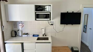 Una cocina compacta con armarios blancos, un microondas, un lavabo, una mesita y un cubo de basura.