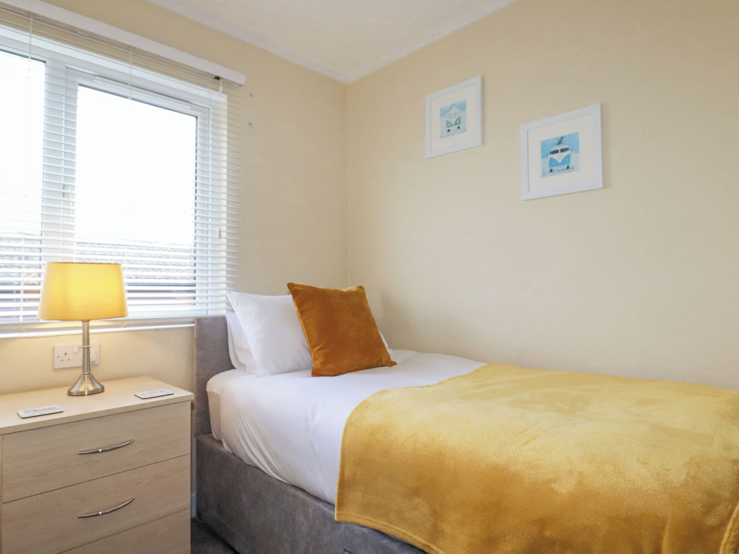 A bedroom with a bed, a bedside table, a lamp, and two framed pictures on the wall.