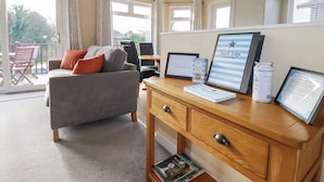 Habitación moderna con sofá gris, escritorio de madera e información para huéspedes enmarcadas.