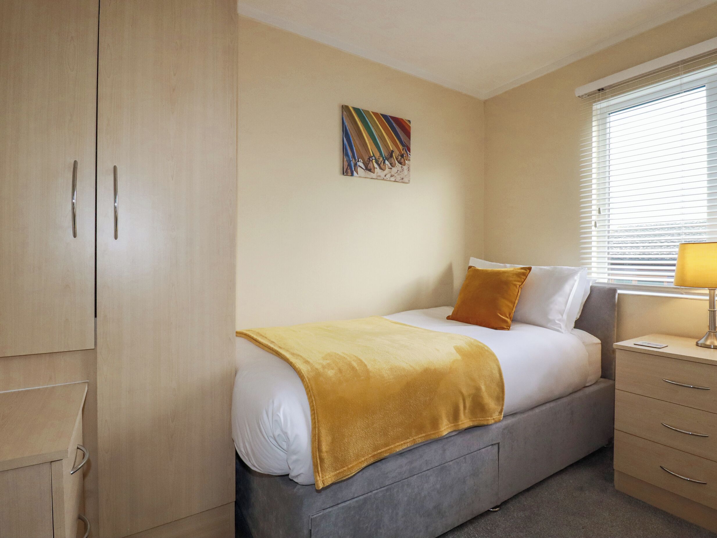 A hotel room with a bed, a bedside table with a lamp, a wardrobe, and a painting on the wall.