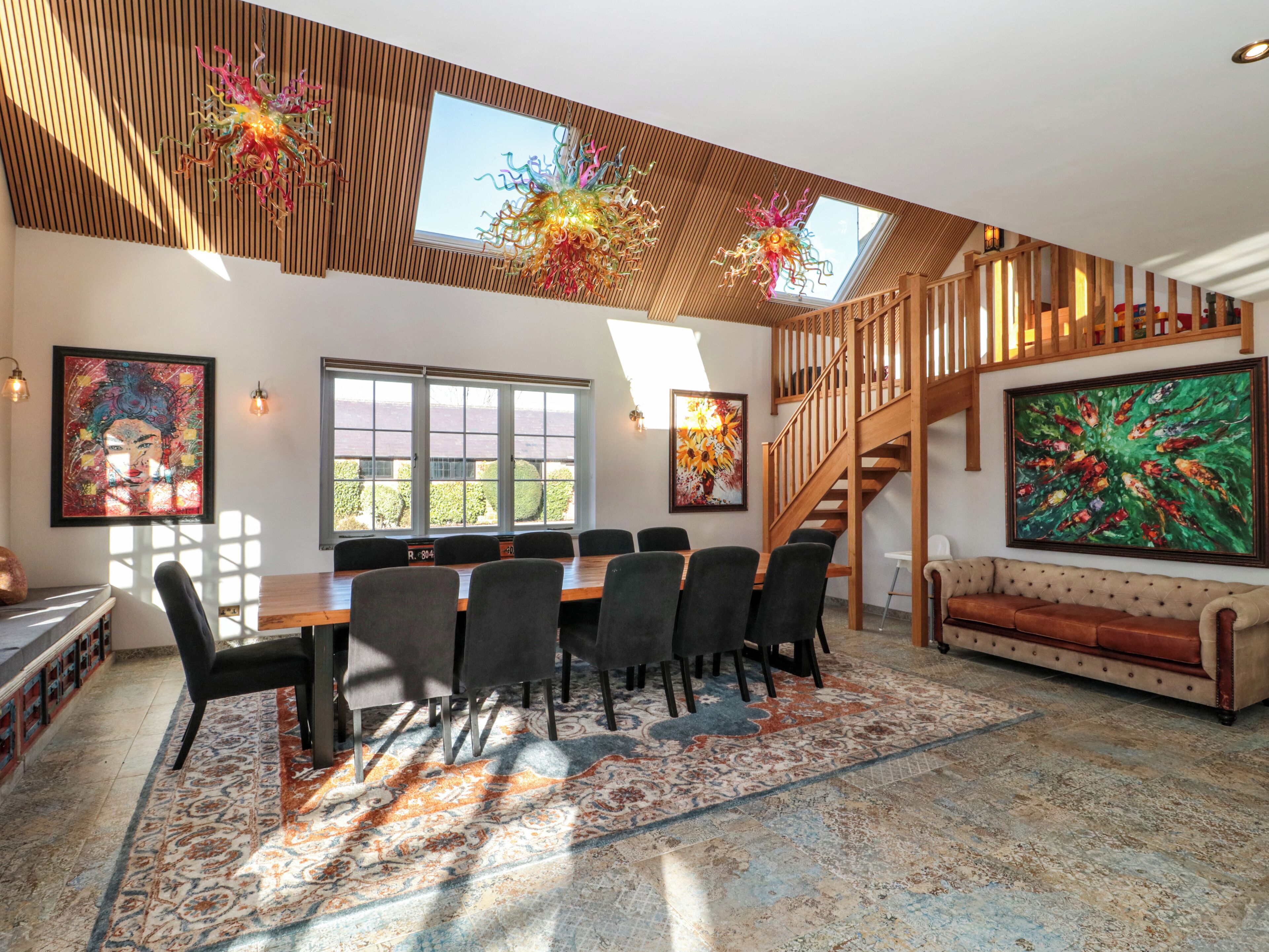A spacious living area with a large dining table, comfortable seating, a staircase, and artwork on the walls.
