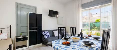 A dining area with a table set for four, a sofa, a TV mounted on the wall, and a view of the outside through large windows.