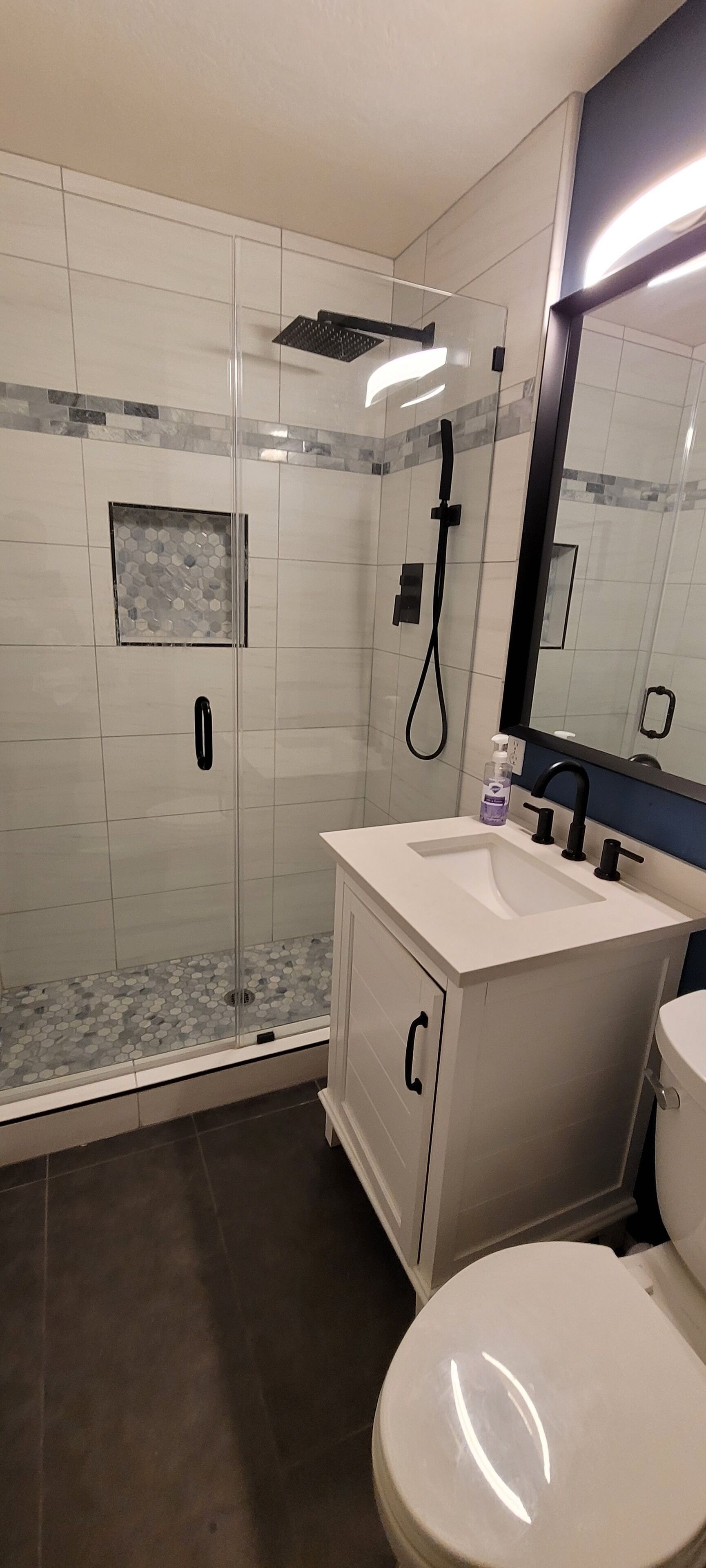 Ein modernes Badezimmer mit einer glasumschlossenen Dusche, einem weißen Waschbecken mit schwarzen Armaturen und einer Toilette.