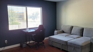 A room with a grey sofa, a black office chair, a small table, and a window with blinds. - 4-bedroom house in delightful Glendale with WiFi, fitness room, AC (Glendale)