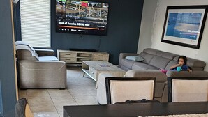 A living room with a dark wooden dining table, a sofa, and a television mounted on the wall. - 4-bedroom house in delightful Glendale with WiFi, fitness room, AC (Glendale)