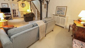 Una sala de estar acogedora con un sofá, un aparador de madera, un televisor y una escalera que sube a otra habitación.