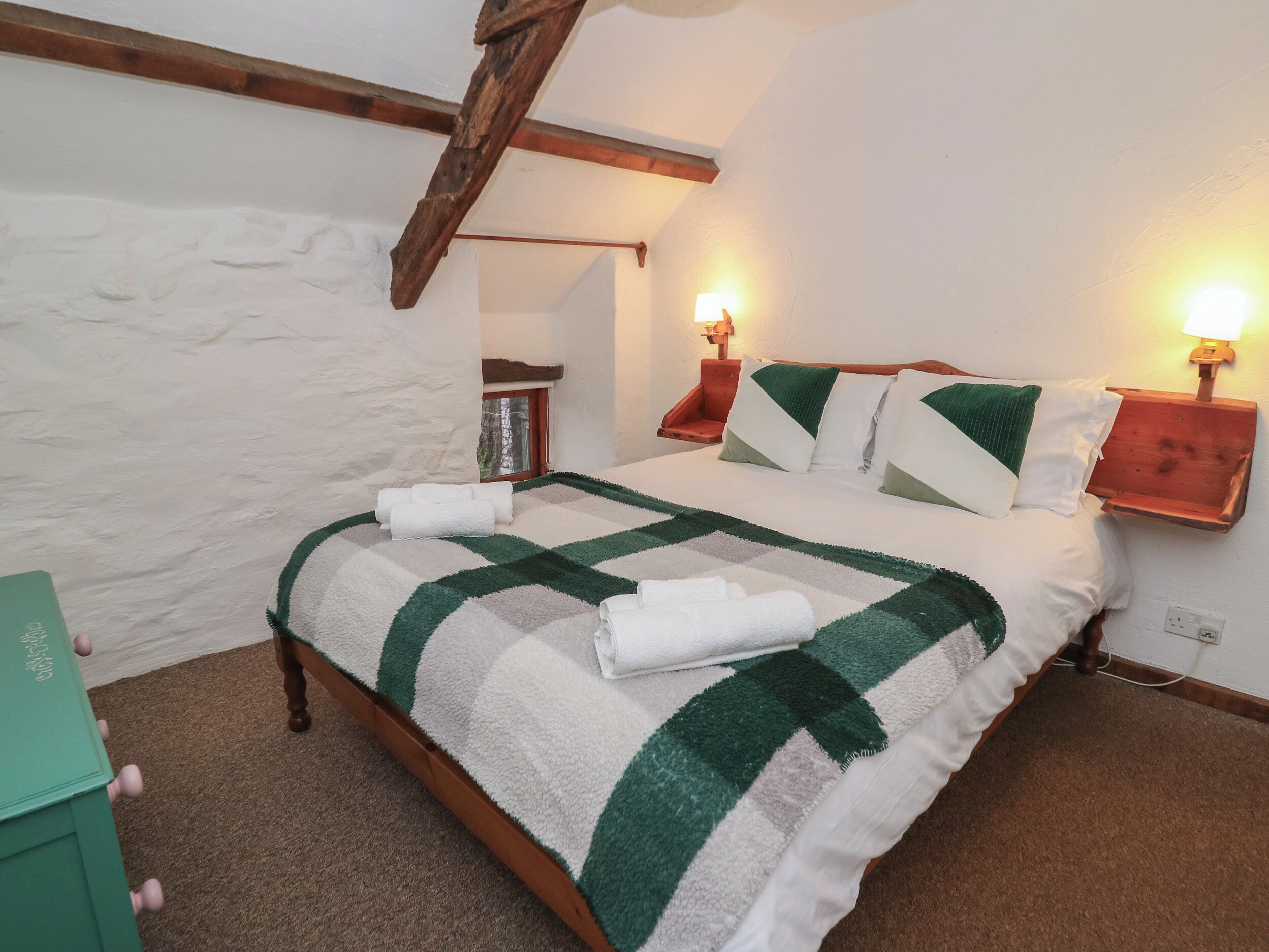 Ein Schlafzimmer mit einem hölzernen Bett, einer grün-weißen Karodecke, zwei Nachttischlampen und einem kleinen Nachttisch.