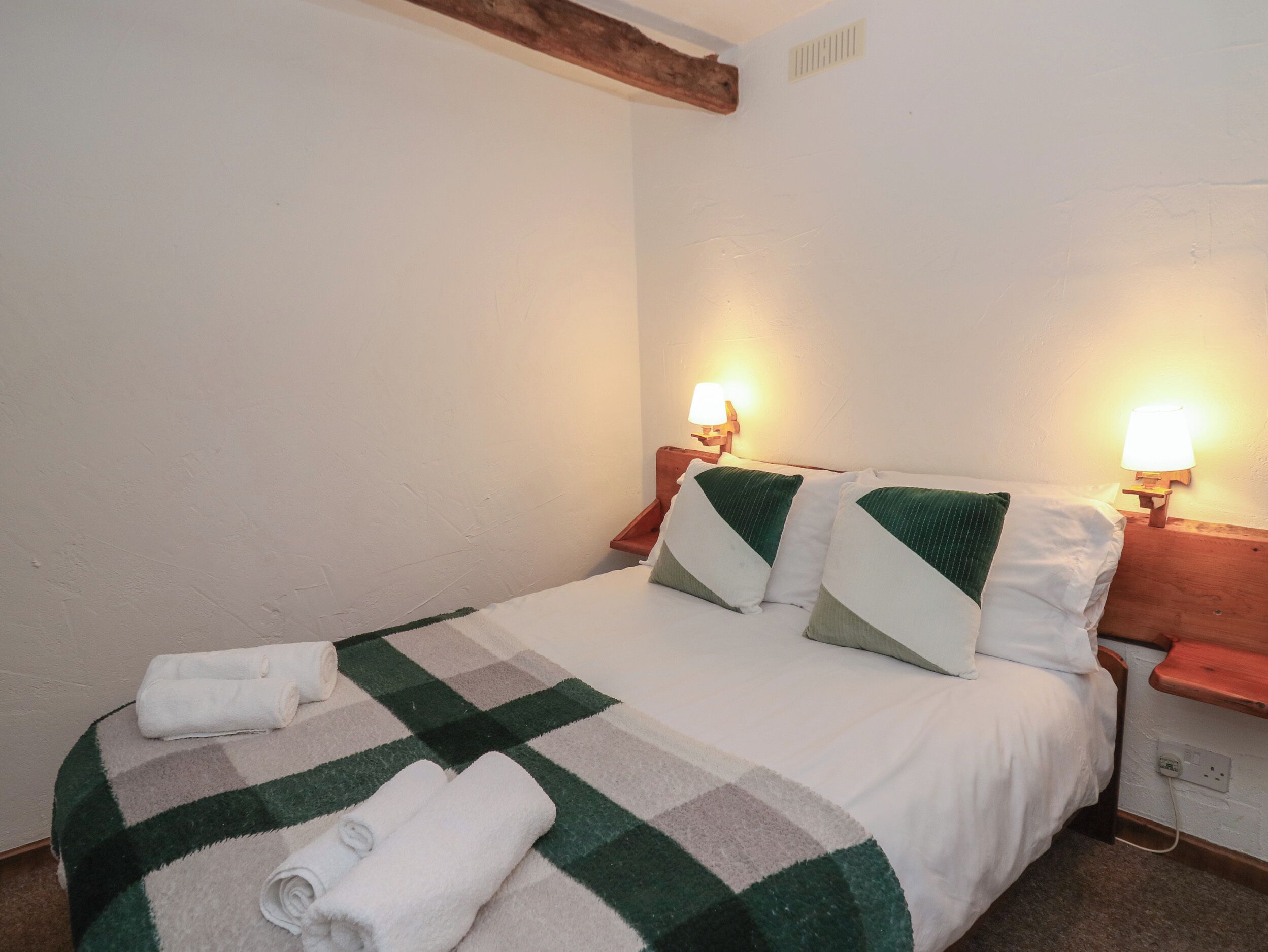 Ein ordentlich bezogenes Bett mit einer karierten Decke, zwei Kissen und zwei Nachttischlampen.