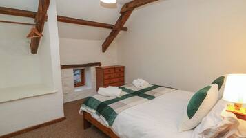 A bedroom with a bed, wooden beams, a dresser, a hanging light fixture, and a small window.