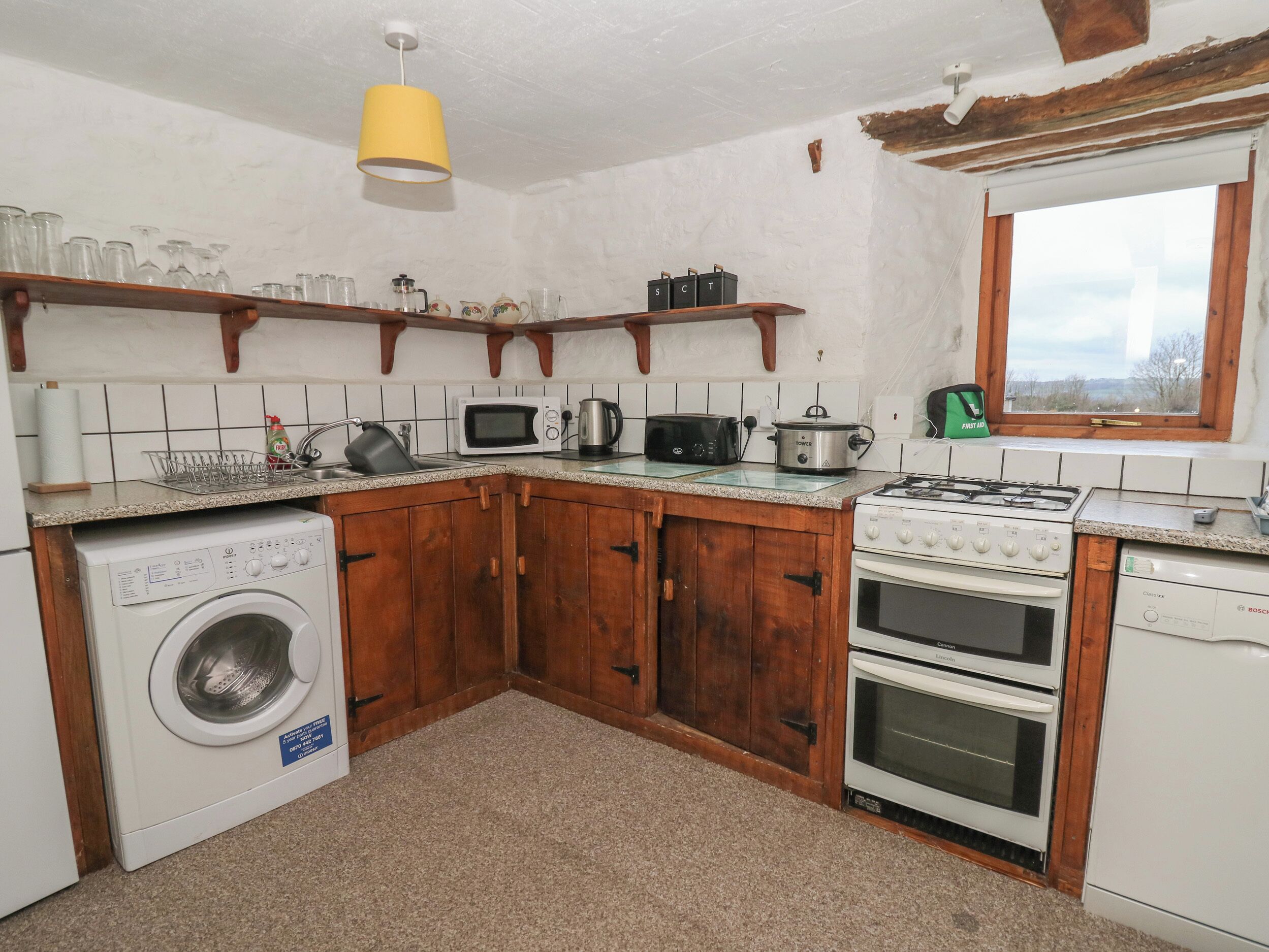 Une cuisine compacte avec des meubles en bois, un lave-linge, un four à micro-ondes, un grille-pain, une cuisinière et une fenêtre donnant sur un beau paysage.